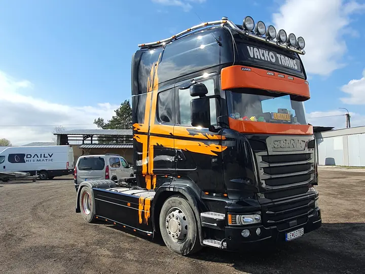 Ťahač Scania s čiernym polepom a oranžovými pruhmi